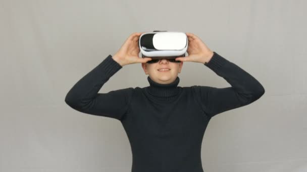 Menino adolescente olha para os óculos de realidade virtual branco ou VR e se diverte em um fundo branco no estúdio. O futuro é agora . — Vídeo de Stock