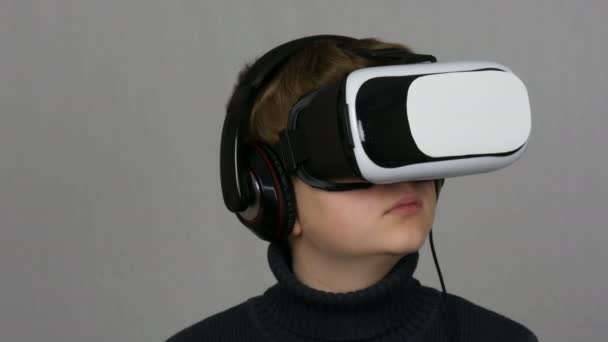 Menino adolescente olha para os óculos de realidade virtual branco ou VR e se diverte em um fundo branco no estúdio. O futuro é agora . — Vídeo de Stock