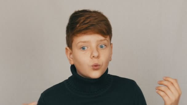 Portré egy vicces vöröshajú és kék szemű tinédzser fiú, bemutatva elítélte a gesztusokat és arckifejezéseket fehér alapon. Tinédzserek érzelmei — Stock videók