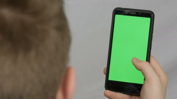 Мальчик-подросток держит в руке черный смартфон с зеленым экраном на белом фоне. Технологии — стоковое видео