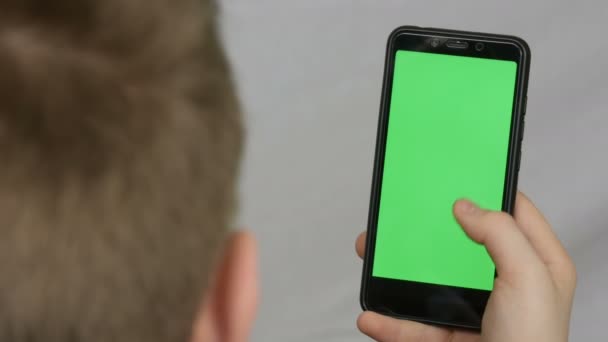 Dospívající mladík má v ruce černý smartphone se zelenou obrazovkou na bílém pozadí. Technologie — Stock video