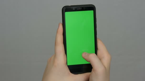 Adolescente menino segura na mão um smartphone preto com uma tela verde no fundo branco. Tecnologia — Vídeo de Stock