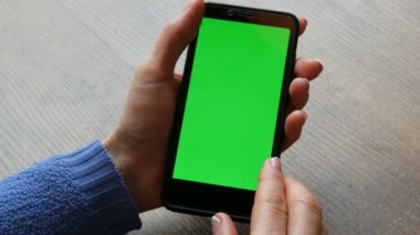 Ahşap masa arka planda iyi bakımlı manikür ile kadın elleri siyah bir smartphone üzerinde Chroma tuşu veya yeşil ekran