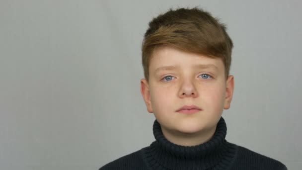 Portrait of a handsome teenager boy with red hair and blue eyes with freckles in a sweater on a white background in studio — Stock Video