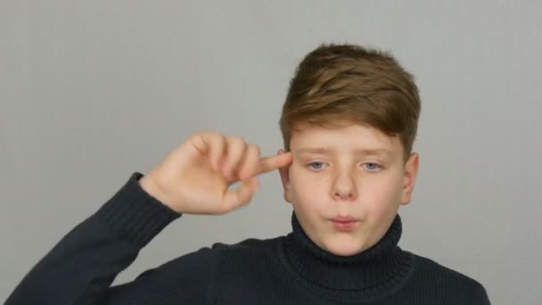 Πορτραίτο έφηβο αγόρι αναστρέφει το δάχτυλό του στο ναό του και φαίνεται κατηγοριμένο σε ένα λευκό φόντο στο στούντιο. Τα συναισθήματα των εφήβων — Αρχείο Βίντεο