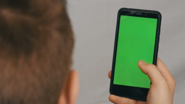De jongen van de tiener houdt in hand een zwarte smartphone met het groen scherm op witte achtergrond. Technologie — Stockvideo