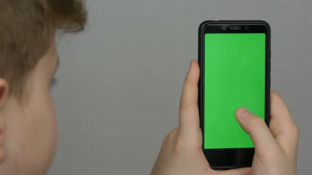 Teen αγόρι κρατά στο χέρι ένα μαύρο smartphone με μια πράσινη οθόνη σε λευκό φόντο. Τεχνολογία — Αρχείο Βίντεο