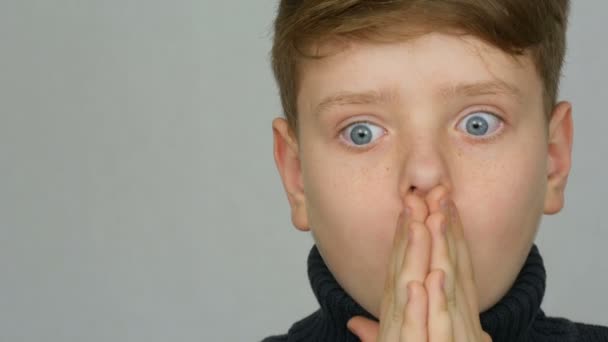 Retrato de um engraçado menino adolescente ruivo com olhos azuis e sardas que é surpreendido em um fundo branco no estúdio — Vídeo de Stock