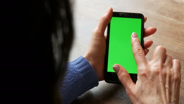 Chroma Key of groen scherm op een zwarte smartphone in vrouwelijke handen met goed verzorgde manicure en zwart haar op de achtergrond van een houten tafel — Stockvideo