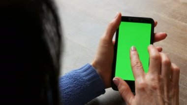 Ahşap bir masa arka planda iyi bakımlı manikür ve siyah saçlı kadın elleri siyah bir smartphone üzerinde Chroma anahtar veya yeşil ekran