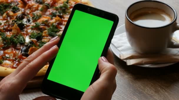 Tecla de croma o pantalla verde en un teléfono inteligente negro en manos femeninas con una manicura bien arreglada en el fondo de una pizza grande y una taza de café — Vídeos de Stock