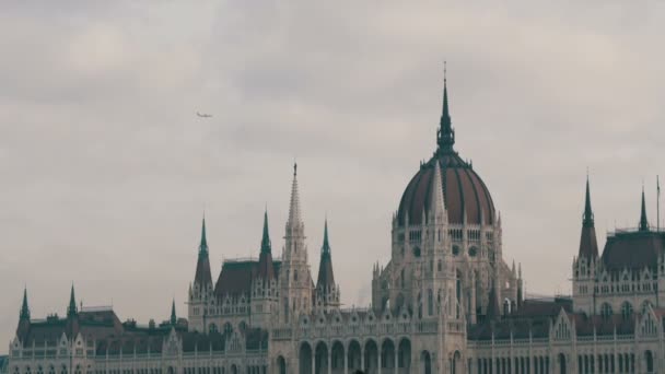 Den världs berömda parlamentsbyggnaden i Budapest byggdes i det gotiska i bakgrunden av ett flyg plan flyger uppifrån i molnigt väder. — Stockvideo