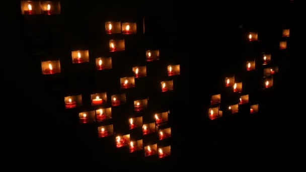 Brûler de belles bougies rondes rouges dans une niche spéciale dans l'obscurité d'une église catholique . — Video