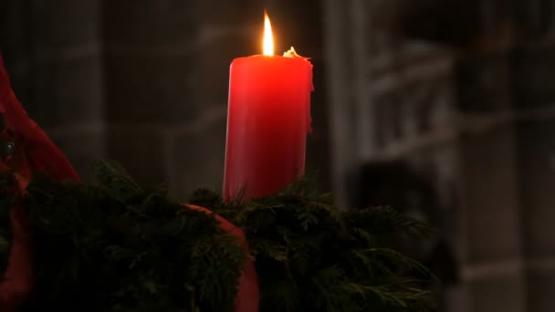 Uma grande vela vermelha de cera queimando sob o teto e de pé em uma grinalda de abeto em uma igreja católica . — Vídeo de Stock