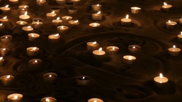 Un gran numero di piccole candele rotonde bianche che bruciano nella sabbia. Sfondo di candele di cera bruciante . — Video Stock