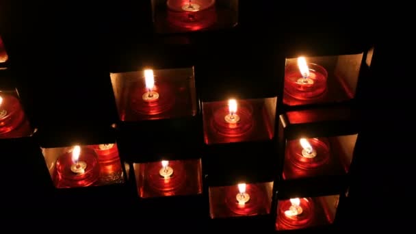 Burning beautiful red round prayer candles in a special niche in the darkness of a Catholic church. — Stock Video