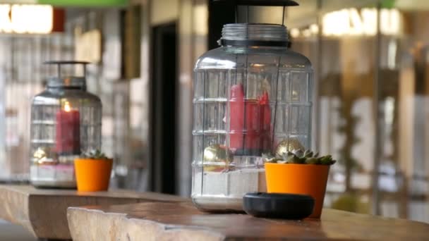 Дві красиві скляні свічки з великою червоною палаючою восковою свічкою червоного кольору, яка знаходиться всередині свічки і стоїть на столі вуличного кафе — стокове відео