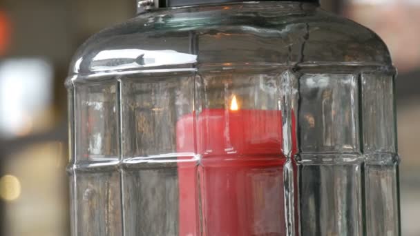 Schöner gläserner Kerzenständer mit einer großen roten brennenden Wachskerze roter Farbe, die sich im Kerzenständer befindet und auf dem Tisch des Straßencafés steht — Stockvideo