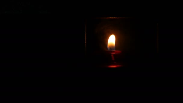 One burning beautiful red round prayer candle in a special niche in the darkness of a Catholic church. — Stock Video