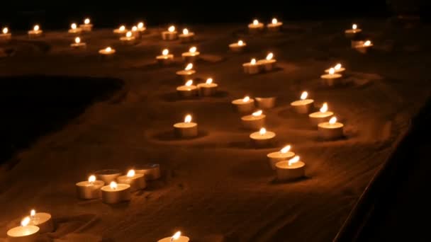 Un grand nombre de petites bougies rondes blanches brûlant dans le sable. Contexte de la combustion des bougies de cire . — Video