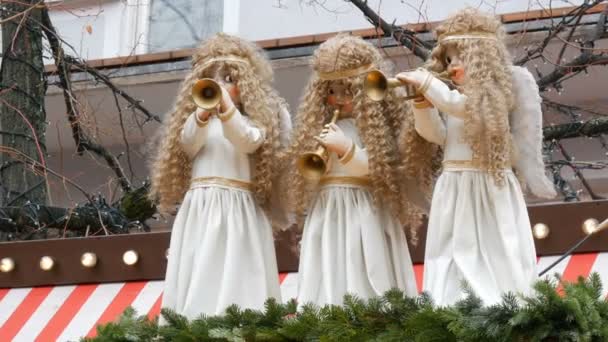 Drei bewegliche Engelspuppen mit Pfeifen in schneeweißen Kleidern auf dem Dach des Kiosks des Kinderweihnachtsmarktes in Europa. — Stockvideo