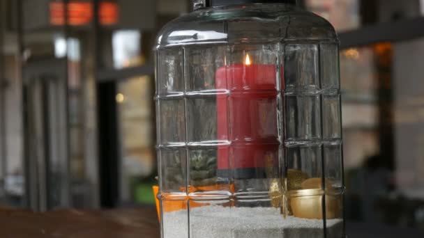 Hermoso candelabro de cristal con una gran vela de cera ardiente roja de color rojo que está dentro del candelabro y se encuentra en la mesa de la cafetería de la calle — Vídeo de stock