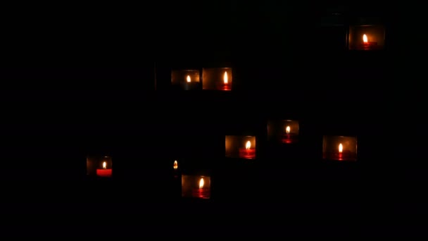 Brûler de belles bougies rondes rouges dans une niche spéciale dans l'obscurité d'une église catholique . — Video