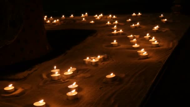 Muitas belas, redondas, pequenas velas brancas queimando na areia no escuro . — Vídeo de Stock