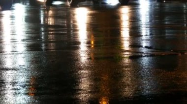 Arabalar trafikte, farlardan asfalt, yağmur altında görüntüleyin. Yağmur su birikintileri geceleri vurur. Arabalar ışıkların yansıması