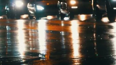 Arabalar trafikte, farlardan asfalt, yağmur altında görüntüleyin. Yağmur su birikintileri geceleri vurur. Arabalar ışıkların yansıması