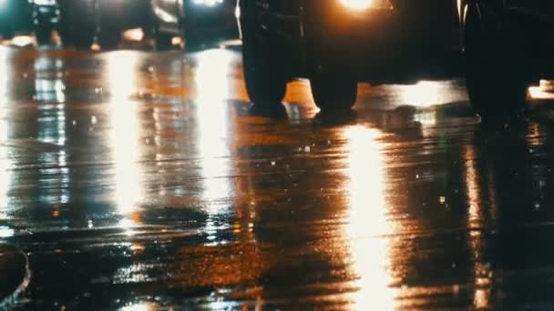 Coches en el tráfico, faros en la lluvia sobre asfalto, vista abajo. La lluvia golpea los charcos por la noche. Reflejo de luces de coches — Vídeo de stock