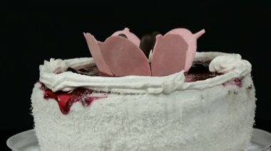 Krem ve Hindistan cevizi yongaları ile üst süslenmiş kiraz reçel ile güzel şık tatlı taze beyaz kek siyah bir arka planda döner.