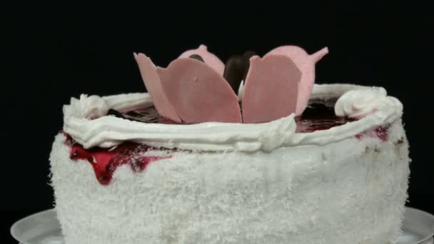 Krásný stylový sladký čerstvý bílý dort se třešňovou marmeládou ozdobenou smetanou a kokosovými čipy se otáčí na černém pozadí. — Stock video