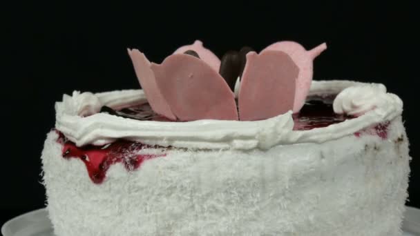 美丽的时尚甜美新鲜的白色蛋糕与樱桃果酱装饰在上面的奶油和椰子片旋转在黑色的背景. — 图库视频影像