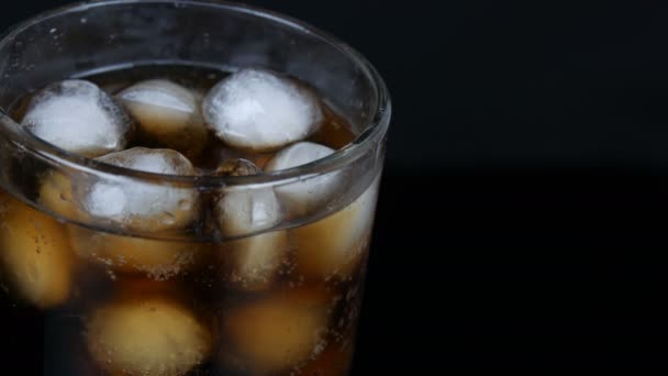 Bolle di cola fredda in un bicchiere lungo trasparente con ghiaccio su fondo nero vista da vicino . — Video Stock