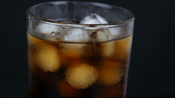 Blasen von kalter Cola in einem transparenten langen Glas mit Eis auf schwarzem Hintergrund Nahaufnahme. — Stockvideo
