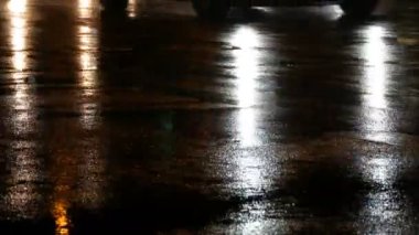 Arabalar trafikte, farlardan asfalt, yağmur altında görüntüleyin. Yağmur su birikintileri geceleri vurur. Arabalar ışıkların yansıması