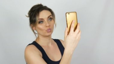 Bir akıllı telefonda bir selfie alır ve beyaz bir arka plana karşı kendini hayran siyah bir elbise güzel bir genç seksi zarif kadın portre