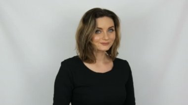 Saç dokunur siyah bir elbise güzel bir genç seksi zarif kadının portresi, saç düzeltir ve beyaz bir arka planda gülümsüyor iken kameraya bakıyor.