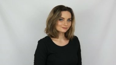Güzel genç seksi kadın siyah elbise onaylayarak sevgi ile nazikçe ve gülümseyerek kamera içine beyaz bir arka planda stüdyo bakıyor.