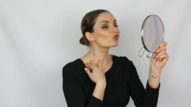 O kendini beyaz bir arka plan üzerinde hayran bakarak ve bir yuvarlak ayna onun elinde tutan güzel zarif seksi genç kadın.