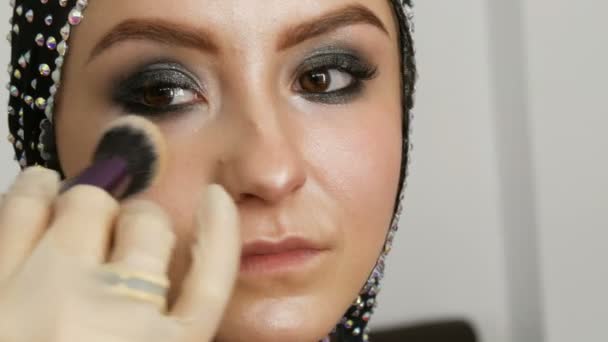 Αναμείξιμες επισημάνετε με επαγγελματική βούρτσα εφαρμόζεται στο πρόσωπο του μοντέλου close up. Νεαρό κορίτσι μοντέλο με όμορφα καστανά μάτια στο στούντιο. Επαγγελματικό make-up από υψηλής μόδας μακιγιάζ καλλιτέχνης — Αρχείο Βίντεο