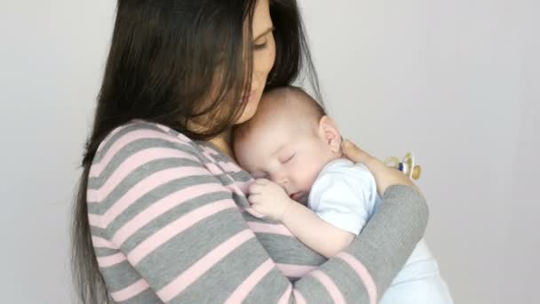 Joven hermosa madre de pelo largo de pelo negro con bebé recién nacido de dos meses que duerme en sus brazos. Mamá acuna a su hijo bebé — Vídeo de stock