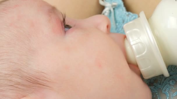 Um bebê recém-nascido de dois meses está nos braços da mãe e suga um mamilo de uma mamadeira de leite. As crianças enfrentam vista de perto — Vídeo de Stock