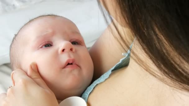 Een mooie jonge langharige moeder zachtjes raakt en wiegt haar pasgeboren baby in armen zittend op haar bed. Close-up van het gezicht childs — Stockvideo