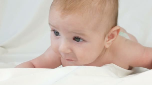 Twee maanden oude gelukkig pasgeboren baby liggend op zijn buik op het bed en ervaringen emoties aan zijn moeder. Een baby lacht, praat, golven zijn armen. Close-up van het gezicht van het kind — Stockvideo