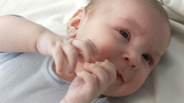 Een twee maanden oude gelukkig pasgeboren baby ligt op het bed en ervaart emoties aan zijn moeder. Een baby lacht, praat, golven zijn armen. Close-up van het gezicht van het kind — Stockvideo