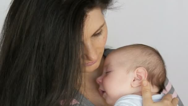 Junge schöne schwarzhaarige langhaarige Mutter mit einem zwei Monate alten Neugeborenen, das in ihren Armen schläft. Mama wiegt ihren kleinen Sohn — Stockvideo