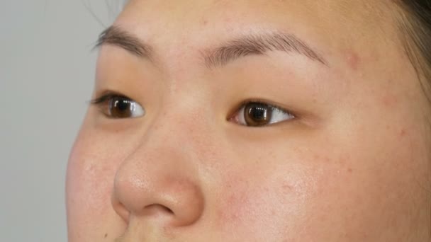 Профессиональный визажист наносит маскировочный макияж специальной кистью на лицо азиатской девушки в визажной студии крупным планом. Высокая мода, съемки видео в студии — стоковое видео