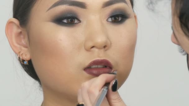 Profesional estilista maquillaje artista compone el ojo humeante de una chica asiática en estudio de visage — Vídeo de stock